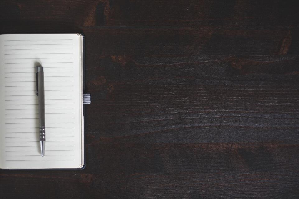 Libreta con un bolígrafo sobre un escritorio de madera oscura
